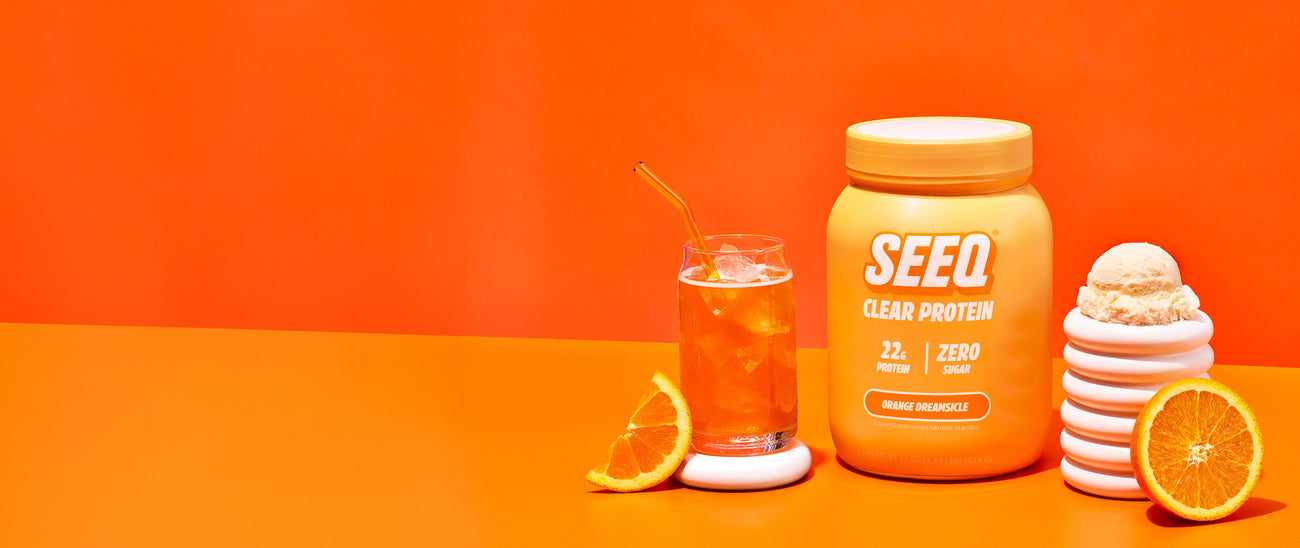 SEED clear protein container with a glass of orange juice and slices on an orange background