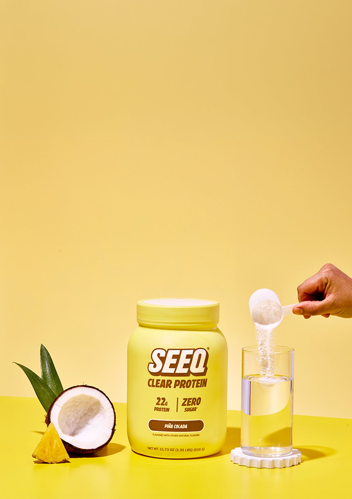 SEEQ Clear Protein container with a scoop and glass of water on a yellow background