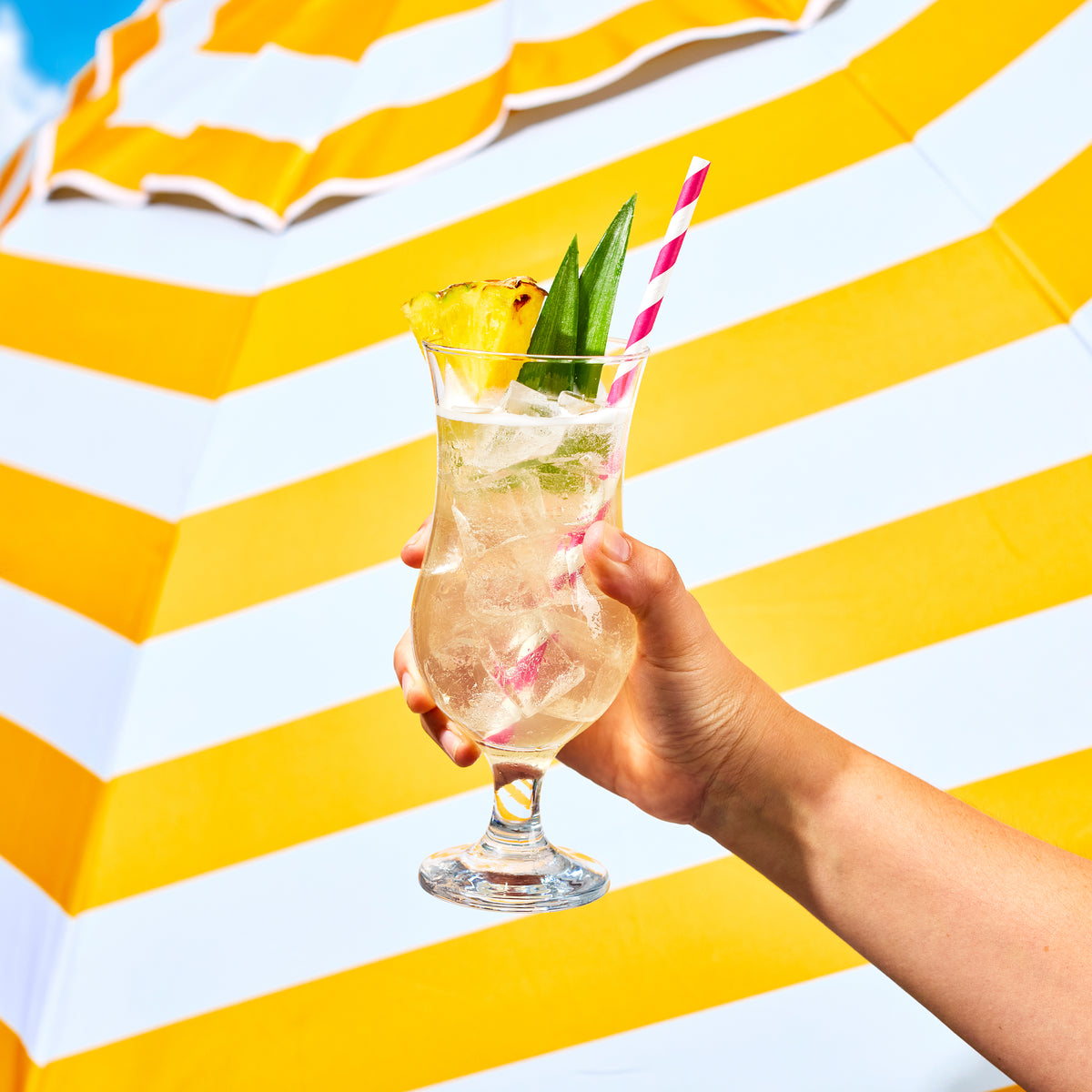 Hand holding a cocktail with a striped yellow and white background