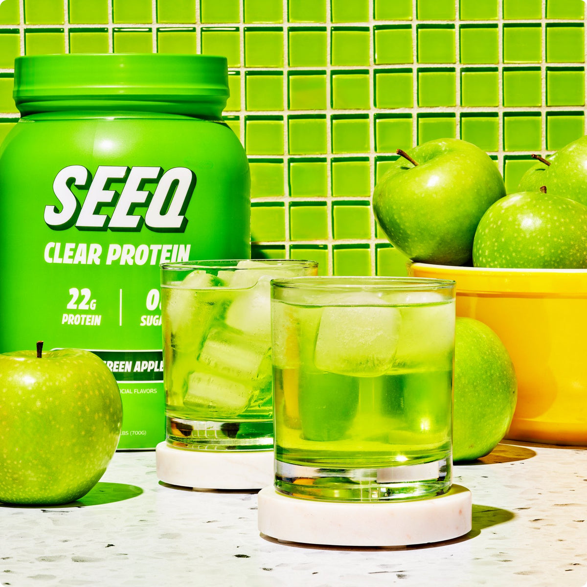 SEEQ Supply’s Sour Green Apple Clear Whey Protein Powder bottle next to a glass of the refreshing, tangy green apple-flavored protein drink.
